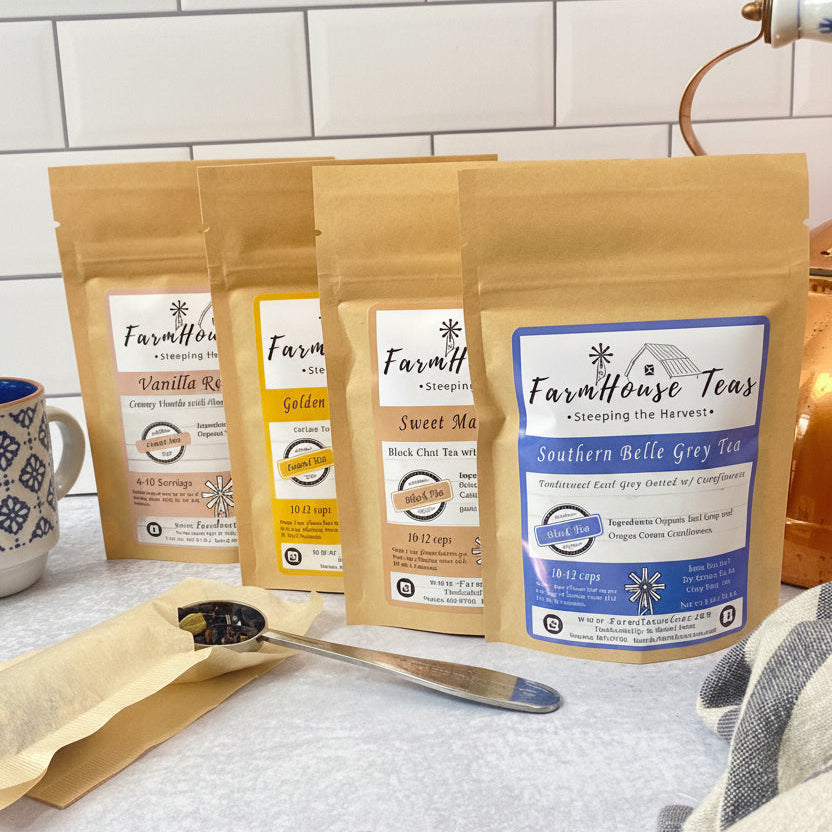 Four stand-up pouches of Farmhouse Teas tea are arranged on a countertop in a kitchen setting, with a white subway tile backsplash behind them. The pouches are in different tea flavors: Vanilla Bean, Lemon, Sweet Tea, and Southern Belle Grey Tea.