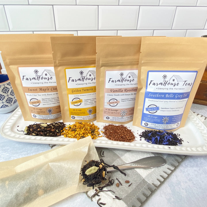 Four stand-up pouches of Farmhouse Tea blends arranged on a white platter with loose tea piles in front, set on a kitchen counter with tiled background.