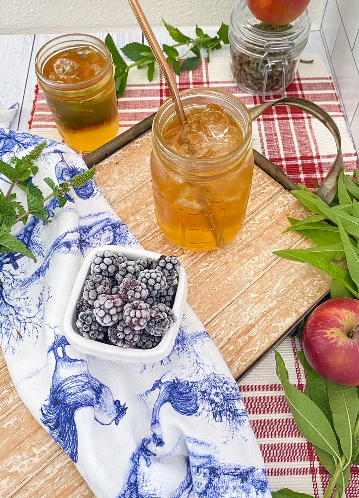 Mason jar with iced tea on a wooden surface with a plaid cloth and berries.
